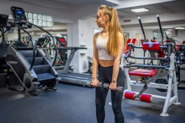 Genç bir kadın elinde dambıllarla spor salonunda egzersiz yapıyor. Yüksek kalite fotoğraf