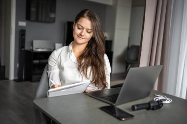 Genç bir kadın iş yerinde dizüstü bilgisayar kullanıyor, notlar yazıyor, kız öğrenci öğreniyor ve çevrimiçi webinar izliyor ya da müzik dersi dinliyor, e-öğrenim eğitim kavramı. Yüksek kalite fotoğraf