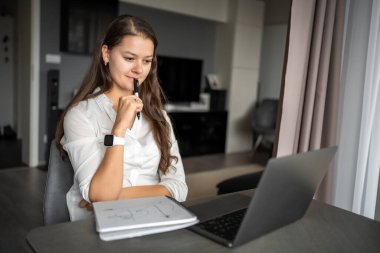 Genç bir kadın iş yerinde dizüstü bilgisayar kullanıyor, notlar yazıyor, kız öğrenci öğreniyor ve çevrimiçi webinar izliyor ya da müzik dersi dinliyor, e-öğrenim eğitim kavramı. Yüksek kalite fotoğraf