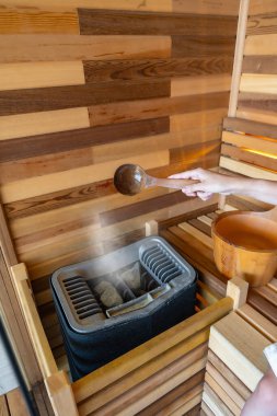 Sauna odasında sıcak taşa su döken bir kadın. Taşlardaki su buharı, spa ve sağlık konsepti. Yüksek kalite fotoğraf