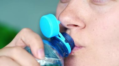 Plastik kapaklı bir şişeden su içen genç bir kadın. Yeni tasarım, açıldıktan sonra kapağın şişeye bağlı kalması ve tüm paketin toplanıp geri dönüşümünün kolaylaştırılması anlamına geliyor.. 