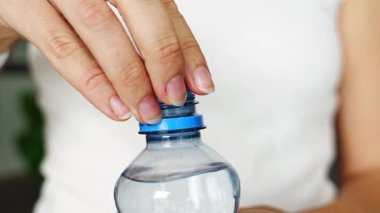 Kadın elinde plastik kapaklı bir şişe. Yeni tasarım, kapağın açıldıktan sonra şişeye bağlı kalması ve tüm paketin toplanıp geri dönüşümünün kolaylaştırılması anlamına geliyor. 4k görüntü