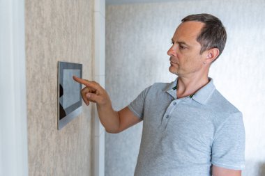 Adam akıllı ev yaşamını kontrol etmek için tablet panel uygulaması kullanıyor. Duvarda ev otomasyonu için kablosuz cihaz kontrolörü var. Yüksek kalite fotoğraf