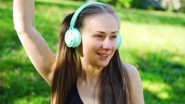 Kablosuz kulaklık takan genç bir kadın şehir parkında müzik dinliyor. Yüksek kalite 4k görüntü