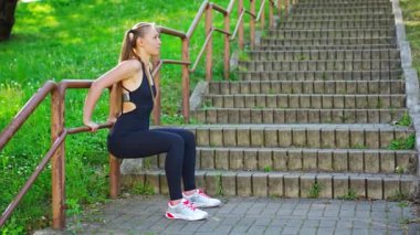 Siyah spor kıyafetli genç bir kadın şehir parkındaki merdivenlerde çömelme egzersizi yapıyor. Açık hava sporları eğitimi konsepti. Yüksek kalite 4k görüntü
