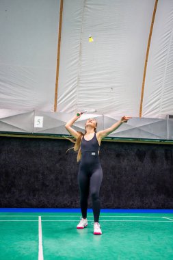 Raket ve mekikle spor yapan genç bir kadın spor yapıyor, iç sahada badminton oynuyor. Yüksek kalite fotoğraf