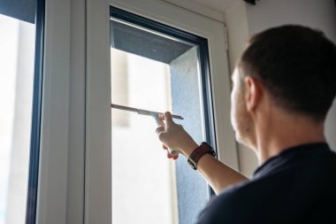 Genç adam evdeki pencereleri temizler. Deterjan sıkar, bardağa su sürer ve temizler. Yüksek kalite fotoğraf