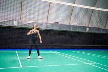 Raket ve mekikle spor yapan genç bir kadın spor yapıyor, iç sahada badminton oynuyor. Yüksek kalite fotoğraf