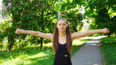 Siyah spor giysili genç bir kadın şehir parkında egzersiz yapıyor. Koşmadan ya da koşmadan önce ısın. Açık hava sporları eğitimi konsepti. Yüksek kalite 4k görüntü