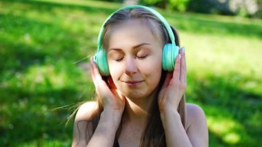Kablosuz kulaklık takan genç bir kadın şehir parkında müzik dinliyor. Yüksek kalite 4k görüntü