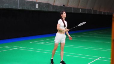 Raket ve mekikle spor yapan genç bir kadın spor yapıyor, iç sahada badminton oynuyor. Yüksek kalite 4k görüntü