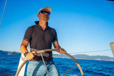 Genç kaptan dümende duruyor ve deniz yolculuğu sırasında bir yelkenliyi kontrol ediyor. Yüksek kalite fotoğraf