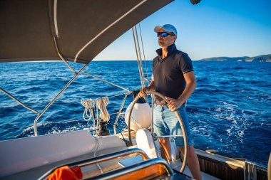 Genç kaptan dümende duruyor ve deniz yolculuğu sırasında bir yelkenliyi kontrol ediyor. Yüksek kalite fotoğraf