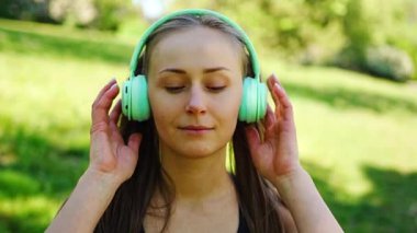 Kablosuz kulaklık takan genç bir kadın şehir parkında müzik dinliyor. Yüksek kalite 4k görüntü