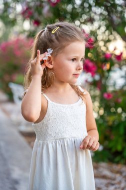 Beyaz elbiseli küçük bir kızın portresi Hırvatistan 'da çiçek açan park geçmişinde mutlu bir şekilde gülümsüyor. Yüksek kalite fotoğraf