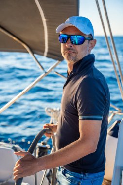 Genç kaptan dümende duruyor ve deniz yolculuğu sırasında bir yelkenliyi kontrol ediyor. Yüksek kalite fotoğraf