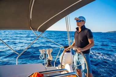 Genç kaptan dümende duruyor ve deniz yolculuğu sırasında bir yelkenliyi kontrol ediyor. Yüksek kalite fotoğraf