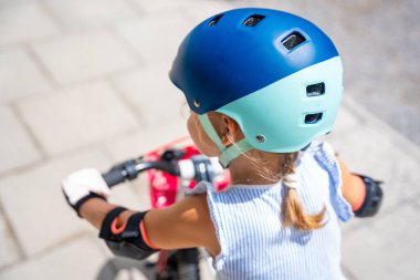 Küçük kızın miğferine yakından bak. Yazın Avrupa 'daki apartmanların avlusunda iki tekerlekli bisiklet sürüyor. Yüksek kalite fotoğraf