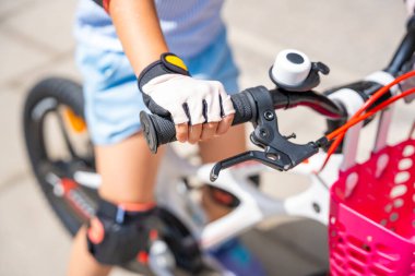 Küçük bir kızın koruyucu eldivenlerini yakından görmek yazın Avrupa 'daki apartmanların avlusunda iki tekerlekli bisiklet sürüyor. Yüksek kalite fotoğraf