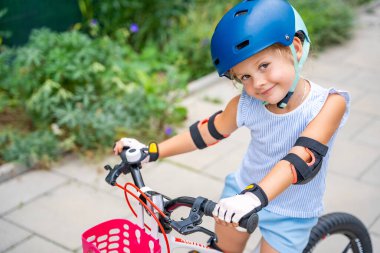 Küçük bir kızın portresi iki tekerlekli bir bisiklete biniyor. Yazın, Avrupa 'da apartmanların avlusunda. Yüksek kalite fotoğraf