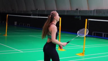 Raket ve mekikle spor yapan genç bir kadın spor yapıyor, iç sahada badminton oynuyor. Yüksek kalite 4k görüntü