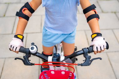 Küçük bir kızın koruyucu eldivenlerini yakından görmek yazın Avrupa 'daki apartmanların avlusunda iki tekerlekli bisiklet sürüyor. Yüksek kalite fotoğraf