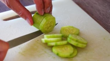 Preparing cucumber for green salad with vegetables, close up view of mans hand in home kitchen. High quality 4k footage