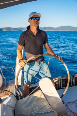 Genç kaptan dümende duruyor ve deniz yolculuğu sırasında bir yelkenliyi kontrol ediyor. Yüksek kalite fotoğraf