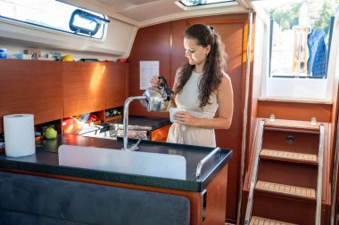 Denizde yelken açarken modern yatın kabininde ayakta duran ve çayı hazırlayan genç bir kadın. Yat hayatı konsepti. Yüksek kalite fotoğraf