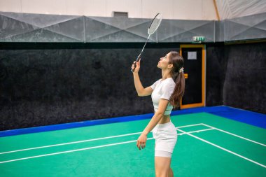 Raket ve mekikle spor yapan genç bir kadın spor yapıyor, iç sahada badminton oynuyor. Yüksek kalite fotoğraf