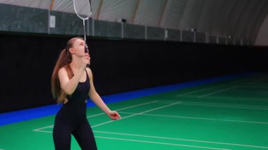 Raket ve mekikle spor yapan genç bir kadın spor yapıyor, iç sahada badminton oynuyor. Yüksek kalite 4k görüntü