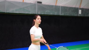 Raket ve mekikle spor yapan genç bir kadın spor yapıyor, iç sahada badminton oynuyor. Yüksek kalite 4k görüntü