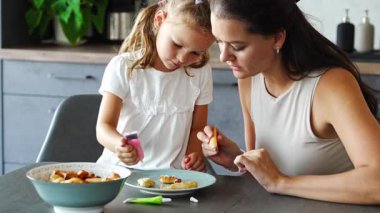 Küçük kız ve annesi ev yapımı kurabiyeleri jölelerle dekore ediyorlar ya da ev mutfağında yemek boyaları, aile hobisi. Yüksek kalite 4k görüntü