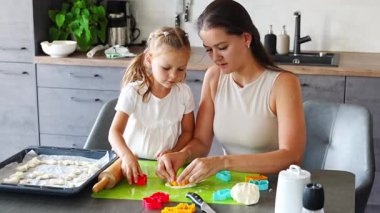 Küçük kız ve annesi ev mutfağında hamurdan kurabiye kalıbı ve kurabiye kalıbı yapıyorlar. Mutfakta mutlu bir aile. Yüksek kalite 4k görüntü