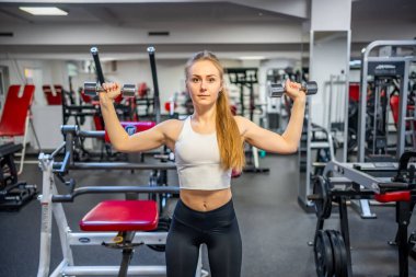 Genç bir kadın elinde dambıllarla spor salonunda egzersiz yapıyor. Yüksek kalite fotoğraf