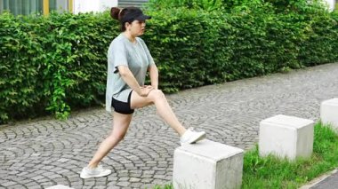 Spor giyimli genç bir kadın şehir caddesinde egzersiz yapıyor. Koşmadan ya da koşmadan önce ısın. Açık hava sporları eğitimi konsepti. Yüksek kalite 4k görüntü