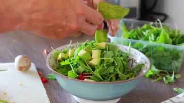 Erkek eller ev mutfağındaki taze salataya avokado ekliyor. Yüksek kalite 4k görüntü