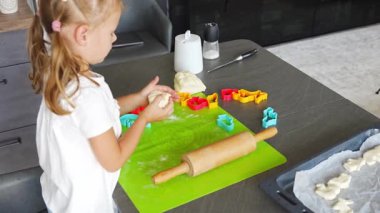 Küçük kız, annesinin hamurla kurabiye yapmasına ve mutfak mutfağında kalıp kalıbı kesmesine yardım ediyor. Mutfakta mutlu bir aile. Yüksek kalite 4k görüntü