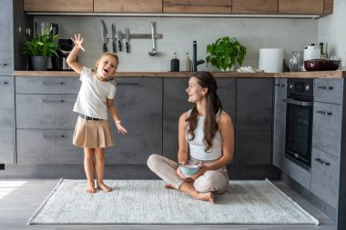 Anne ve kızı mutfak zemininde oturuyor, yemek yiyor ya da kahvaltı edip oynuyorlar. Aile bağı. Yüksek kalite fotoğraf