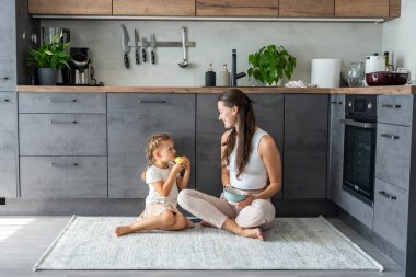 Anne ve kızı mutfak zemininde oturuyor, yemek yiyor ya da kahvaltı edip oynuyorlar. Aile bağı. Yüksek kalite fotoğraf