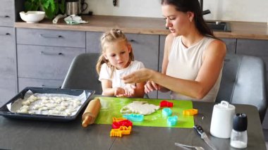 Küçük kız ve annesi ev mutfağında hamurdan kurabiye kalıbı ve kurabiye kalıbı yapıyorlar. Mutfakta mutlu bir aile. Yüksek kalite 4k görüntü