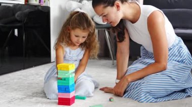 Annesiyle birlikte evde Jenga oyunu oynayan küçük bir kız, ahşap kuleden renkli bloklar alıyor. Yüksek kalite 4k görüntü