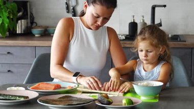 Genç bir anne ve küçük kızı mutfaktaki masada suşi yapıyor. Yüksek kalite 4k görüntü