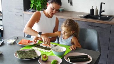 Genç bir anne ve küçük kızı mutfaktaki masada suşi yapıyor. Yüksek kalite 4k görüntü