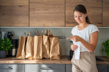 Mutfakta içi yiyecek dolu kağıt torbaların yanındaki dükkandan alınmış fişi olan genç bir kadın. Yiyecekler internetten sipariş edildi ve kuryeyle teslim edildi. Yüksek kalite fotoğraf