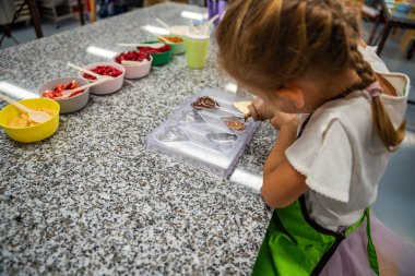 Yemek kursunda yemek yapmayı öğrenen küçük bir kız. El yapımı tatlı. Çikolatalı şeker yapmak, çocuk kalp şeklindeki kalıbı çikolatayla doldurmak. Yüksek kalite fotoğraf