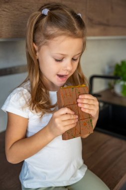 Little girl eating Dubai chocolate with pistachio paste and kataifi dough. Confectionery handmade sweets at home in the kitchen. High quality photo clipart