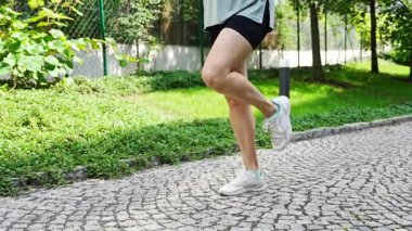 Şehir parkında ayak ve bacak egzersizi yapan genç bir kadının yakın çekim görüntüsü. Koşmadan ya da koşmadan önce ısın. Açık hava sporları eğitimi konsepti. Yüksek kalite 4k görüntü