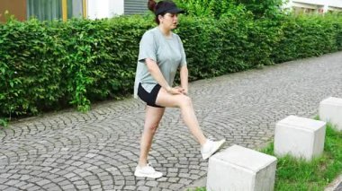 Spor giyimli genç bir kadın şehir caddesinde egzersiz yapıyor. Koşmadan ya da koşmadan önce ısın. Açık hava sporları eğitimi konsepti. Yüksek kalite 4k görüntü