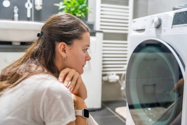 Çamaşır makinesinin bitmesini bekleyen genç bir kadın çamaşır makinesinin kapısına bakıyor. Yüksek kalite fotoğraf
